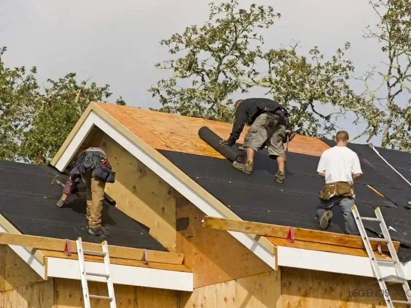Roofing crew rolling underlayment across a new roof deck